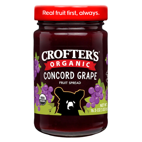 Jar of Crofter's Organic Concord Grape Premium Fruit Spread with fresh grapes and spreading on bread.
