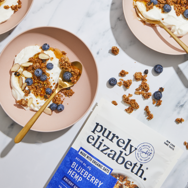Purely Elizabeth Blueberry Hemp Ancient Grain Granola in a bowl with blueberries and hemp seeds, showcasing healthy breakfast ingredients.