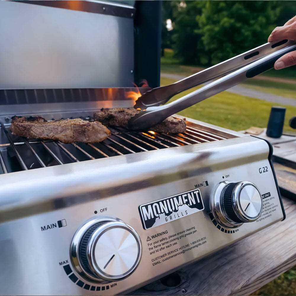 Stainless Monument Grills G22 tabletop propane gas grill with cooking surface and side shelf, ideal for outdoor cooking.
