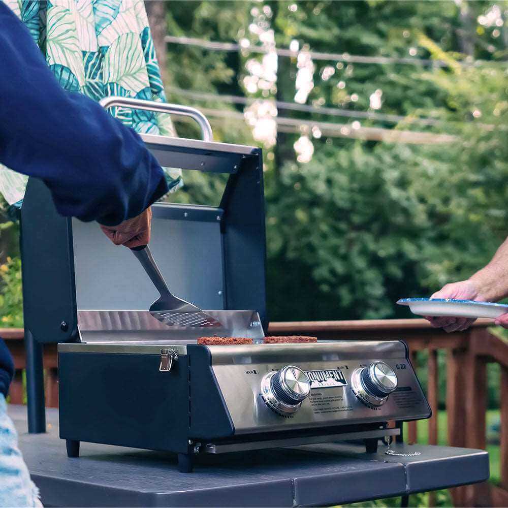 Stainless G22 Monument Grills tabletop propane gas grill with cooking surface and control knobs, perfect for outdoor grilling.
