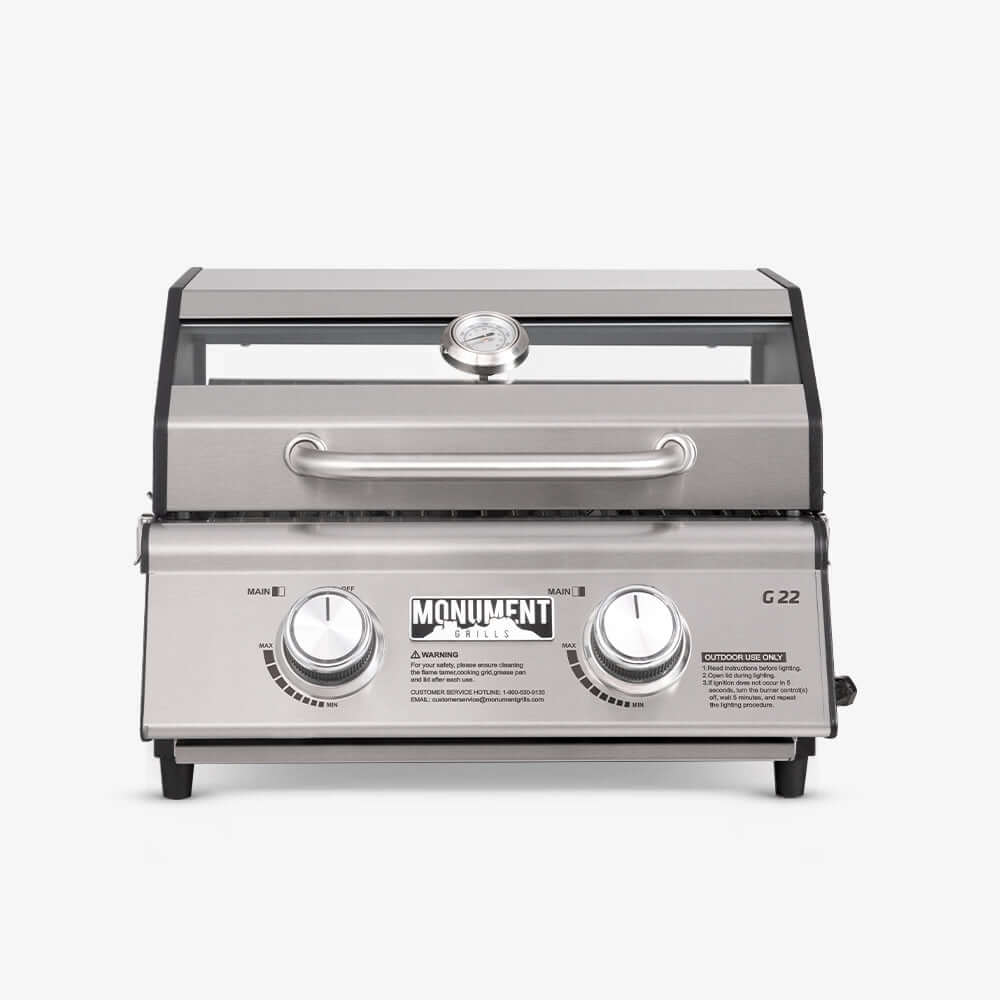 Stainless G22 Monument Grills tabletop propane gas grill with cooking grates and control knobs on a kitchen countertop.