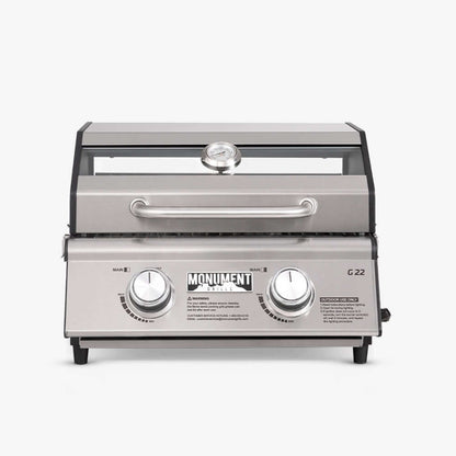Stainless G22 Monument Grills tabletop propane gas grill with cooking grates and control knobs on a kitchen countertop.