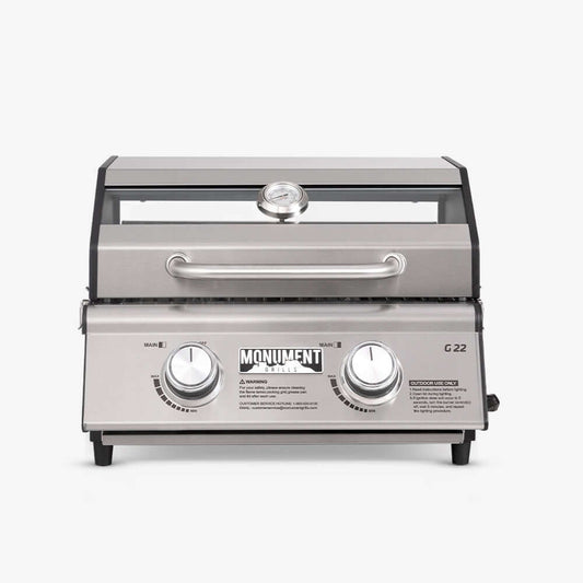 Stainless G22 Monument Grills tabletop propane gas grill with cooking grates and control knobs on a kitchen countertop.