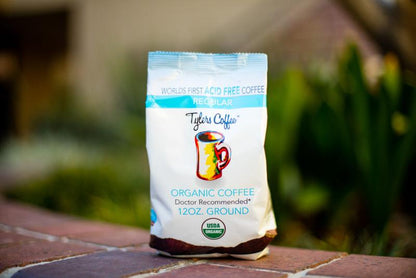 Bag of Tylers Coffees regular acid-free ground coffee with a rustic label and a scoop of coffee grounds on a wooden surface.