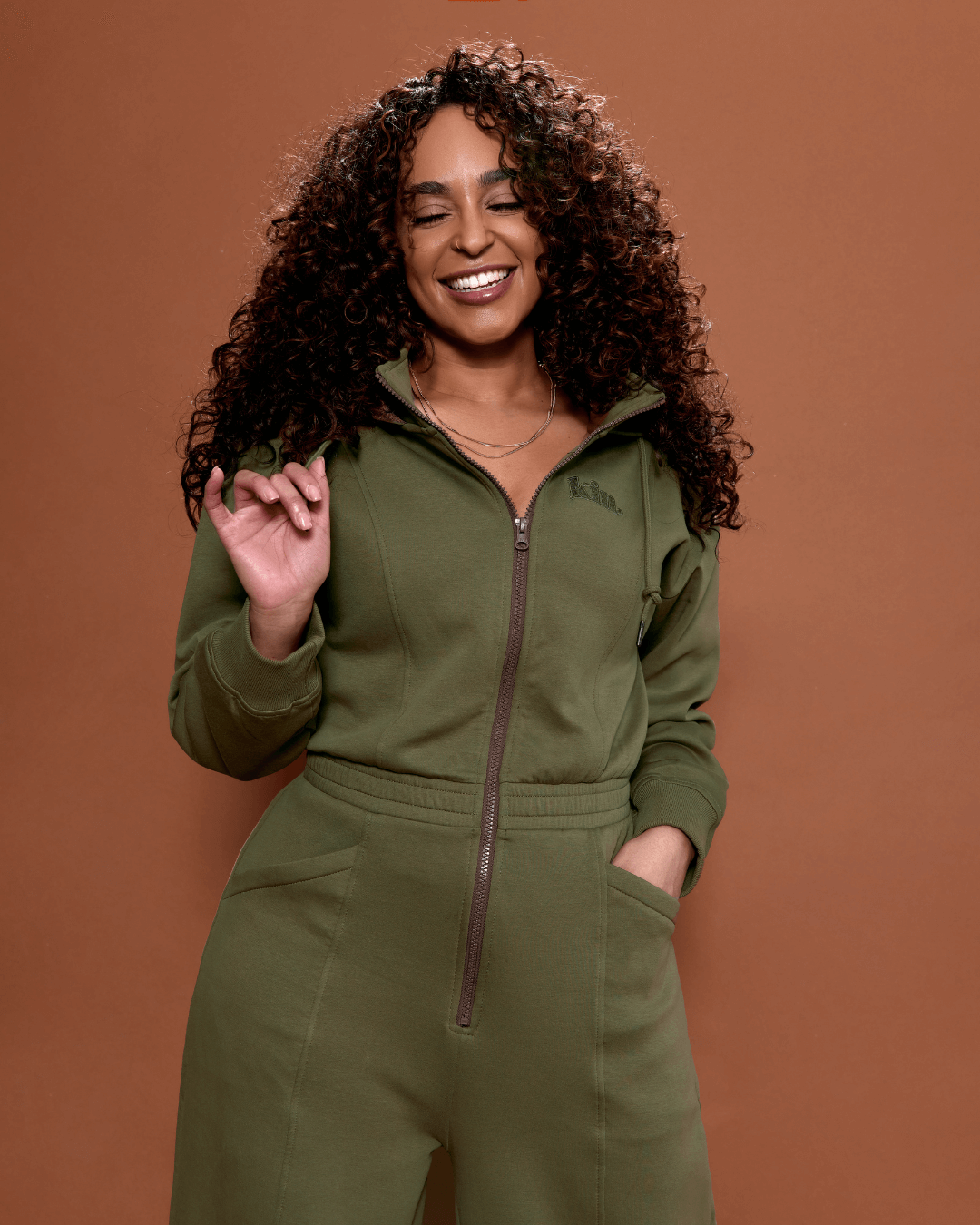 Green satin-lined jumpsuit by KINApparel, showing the fitted design, long sleeves, and smooth satin fabric detail.