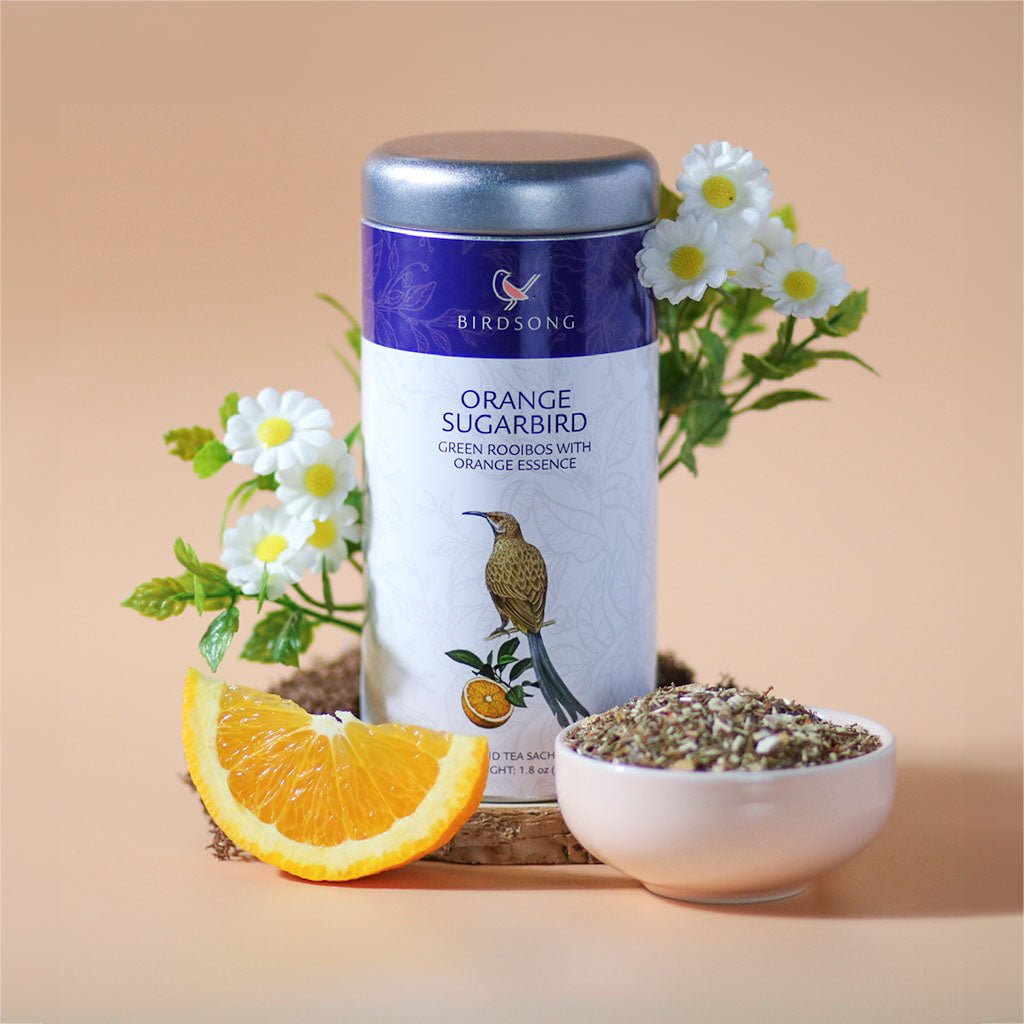 Orange Sugarbird herbal tea by Birdsong Tea featuring vibrant orange and green rooibos leaves in a steaming cup.