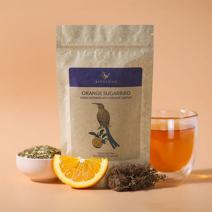 Orange Sugarbird herbal tea by Birdsong Tea featuring vibrant orange and green rooibos tea leaves in a clear cup.