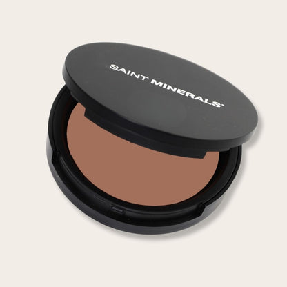 Warm-toned pressed powder foundation from Saint Minerals by Panoply Beauty, showing a compact with smooth, pressed powder surface.