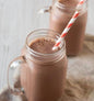 AmBari Nutrition Protidiet Chocolate Shake in a glass, showing a creamy chocolate shake with a straw and fresh chocolate pieces.