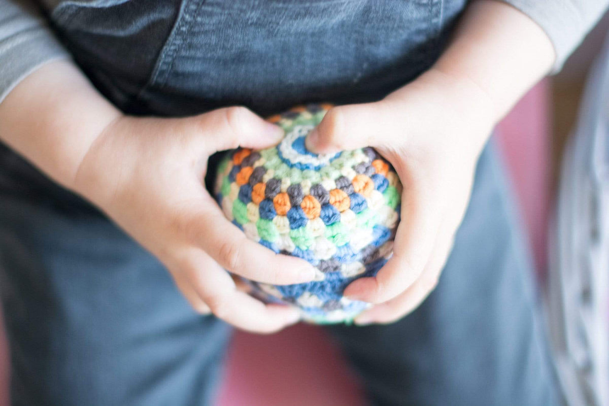 Handmade rainbow rattle ball toy made of organic cotton with colorful stripes, perfect for babies and sensory play.